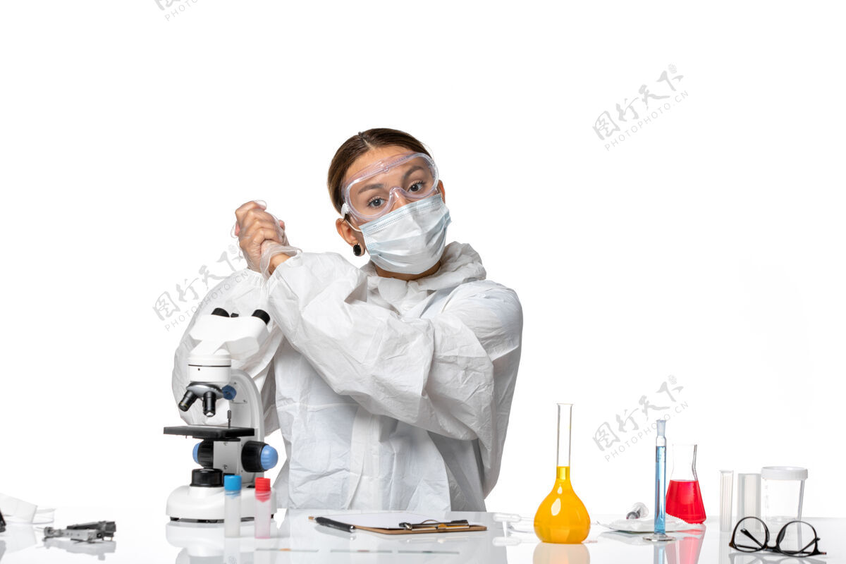 视图正面图女医生穿着特制的西装 戴着口罩 坐在浅白背景上解冠状病毒大流行大流行病毒医疗