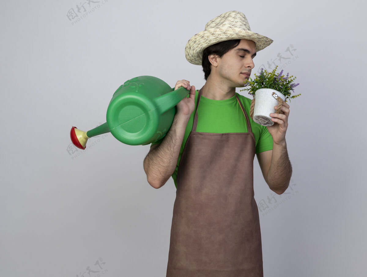 戴穿着制服的年轻男园丁高兴地戴着园艺帽 肩上扛着水罐 在花盆里嗅着花园艺花园男人