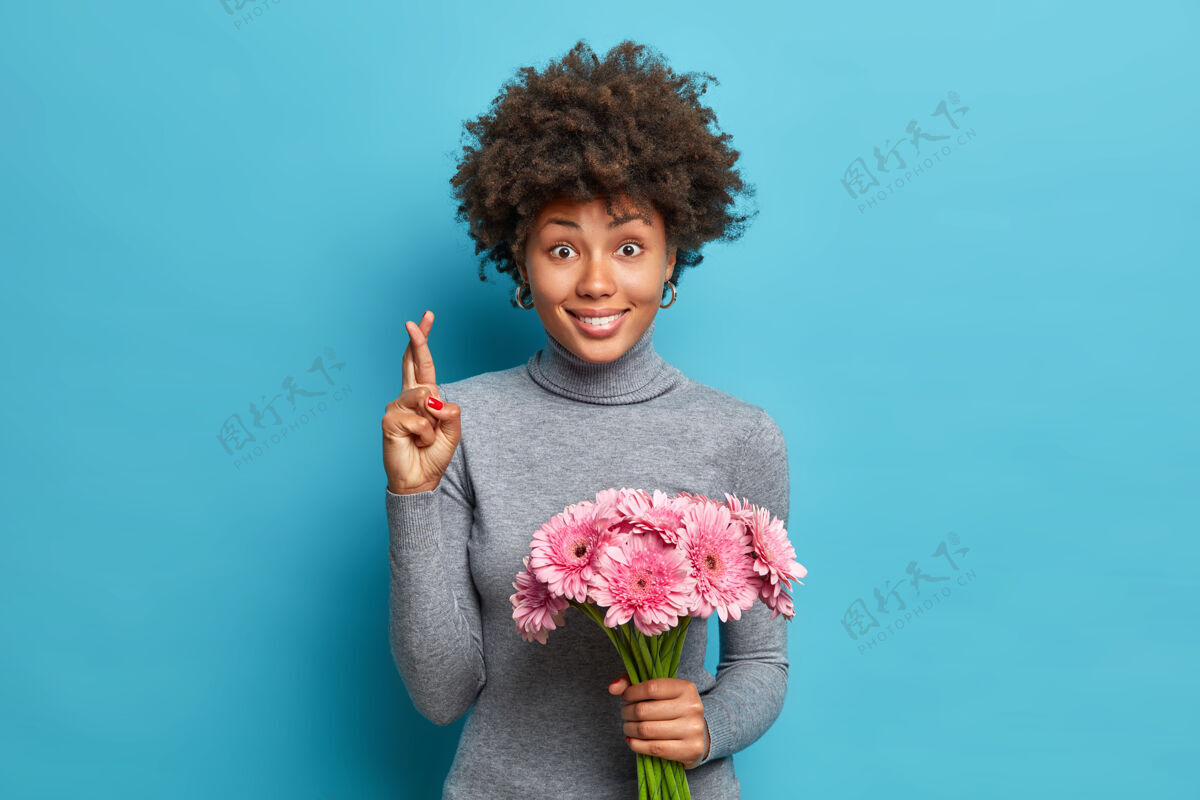 束积极的非裔美国人的肖像十字架手指相信梦想成真持有粉红色非洲菊花束浪漫开花庆祝