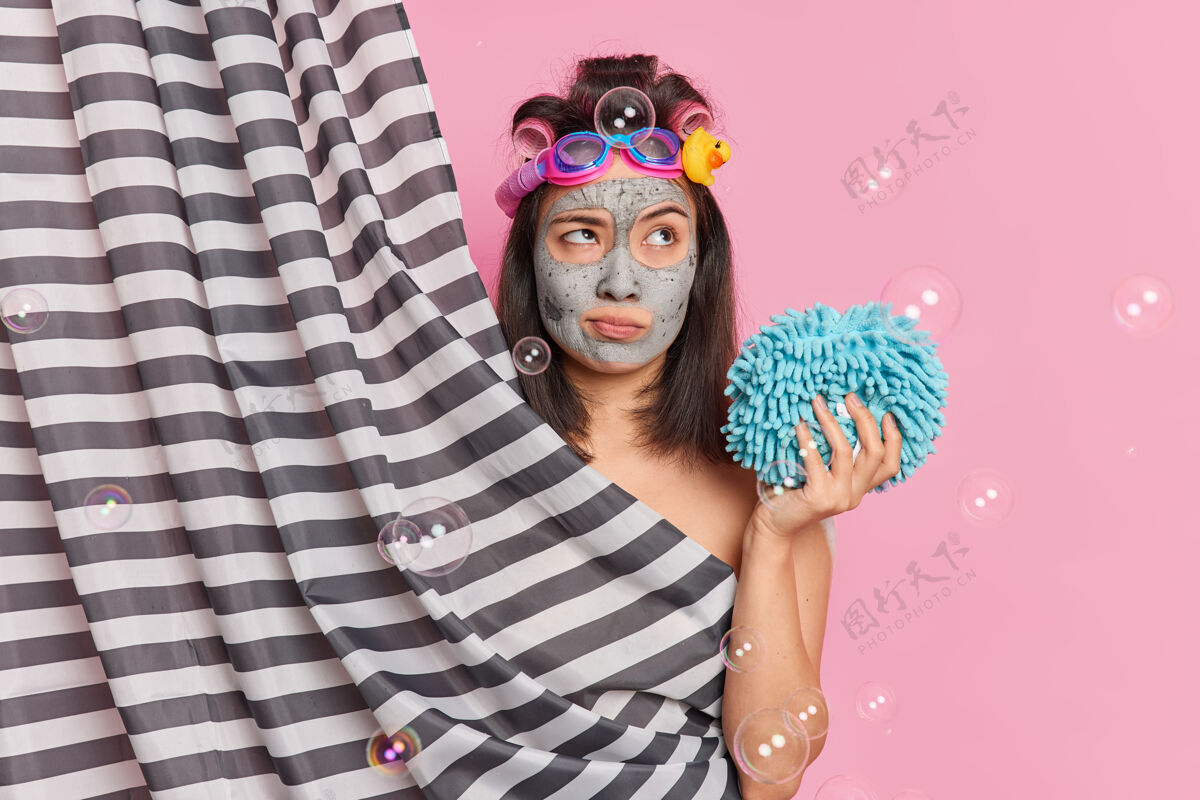 条纹体贴的亚洲女人用泥塑做发型 用发夹拿着浴巾 在粉色的工作室背景下 在窗帘后摆出灌洗姿势 有着深刻的思想姿势女人护理