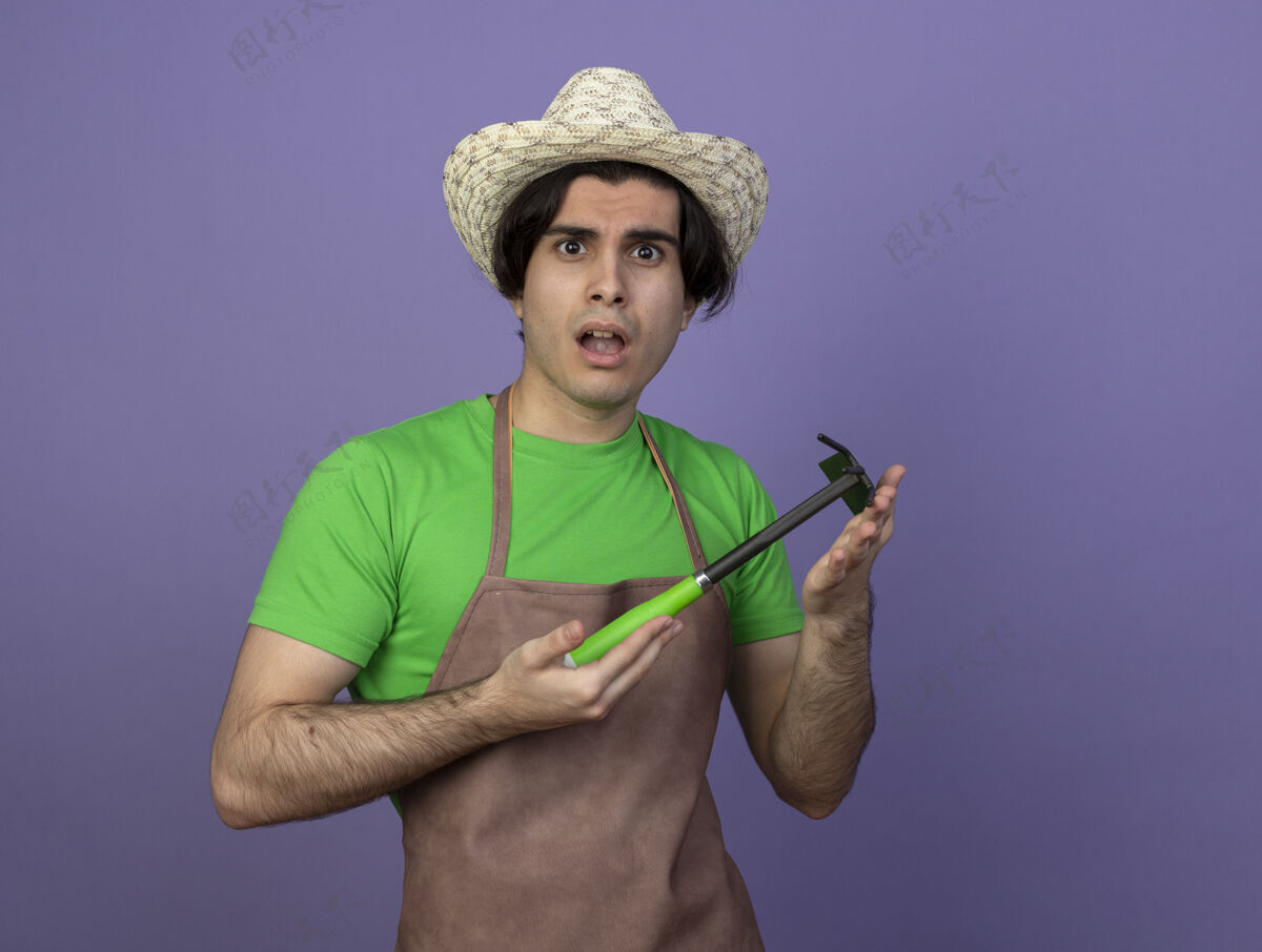 耙子困惑的年轻男园丁穿着制服戴着园艺帽手持锄头耙子制服紫色男性