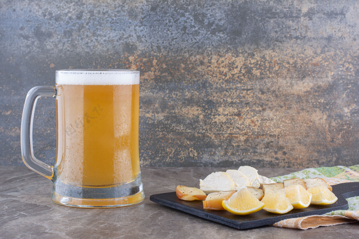 啤酒各种各样的奶酪和柠檬片放在深色的木板上 配上啤酒泡沫提神奶酪