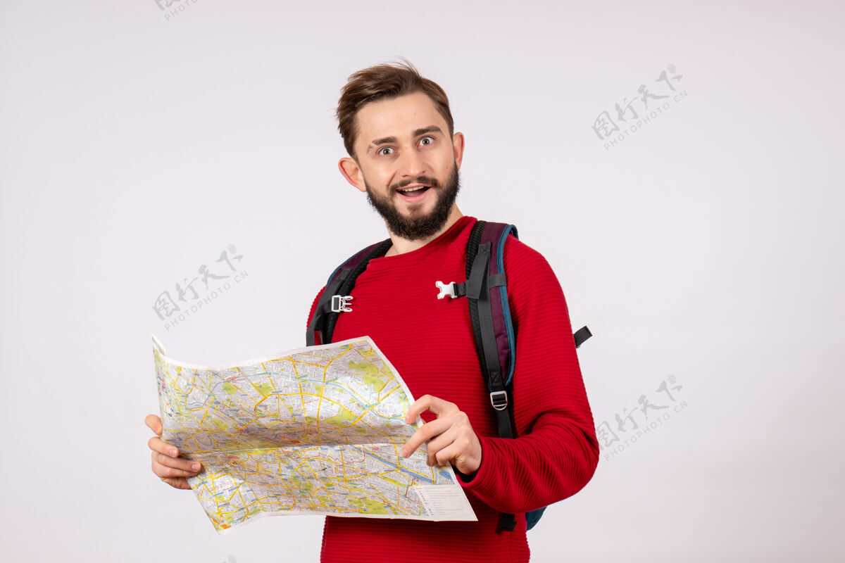 游客正面图：年轻男性游客背着背包在白色墙壁上探索地图covid飞机度假情感病毒飞行色彩病毒微笑情感