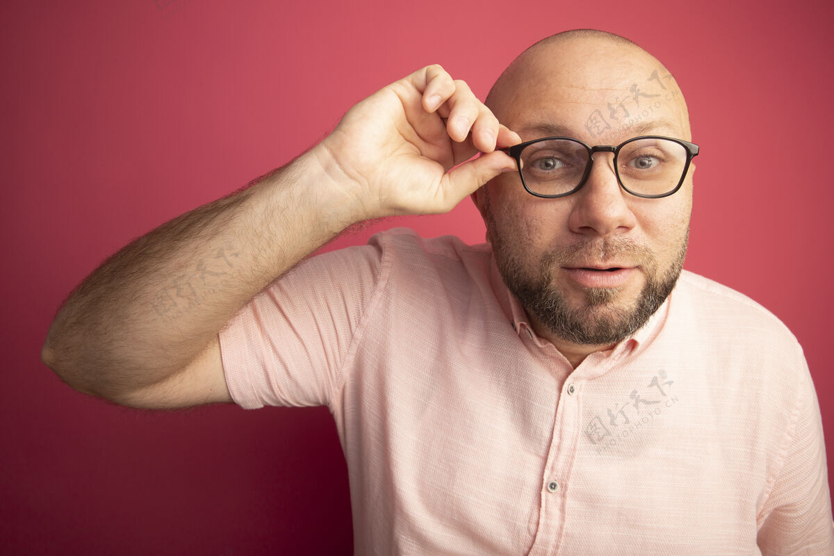 秃头可疑的中年秃头男子穿着粉色t恤 戴着和举着眼镜隔离在粉色墙上可疑男人戴着