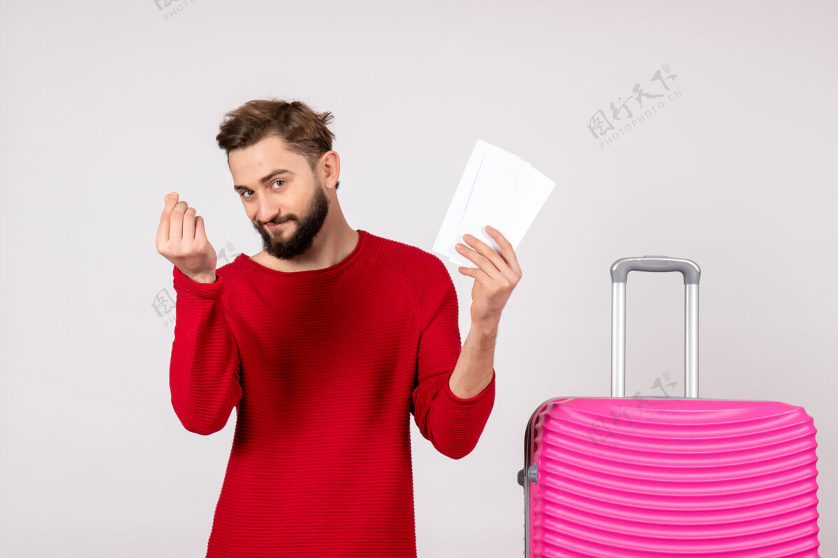 颜色正面图：年轻男性 带着粉红色的包 拿着机票 在白色的墙壁上航行 彩色旅行 旅游度假照片美丽风景肖像