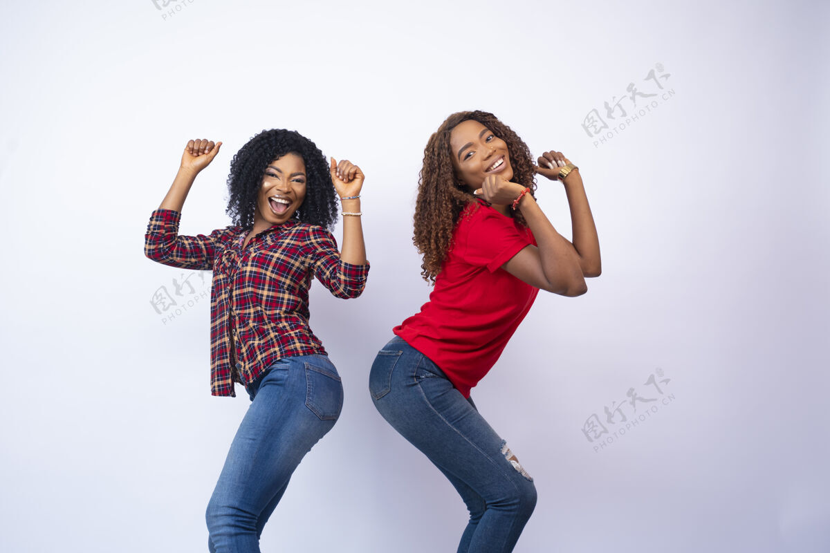 在一起特写两个兴奋的年轻黑人妇女感到高兴和跳舞 在白色背景前欢呼友谊休闲