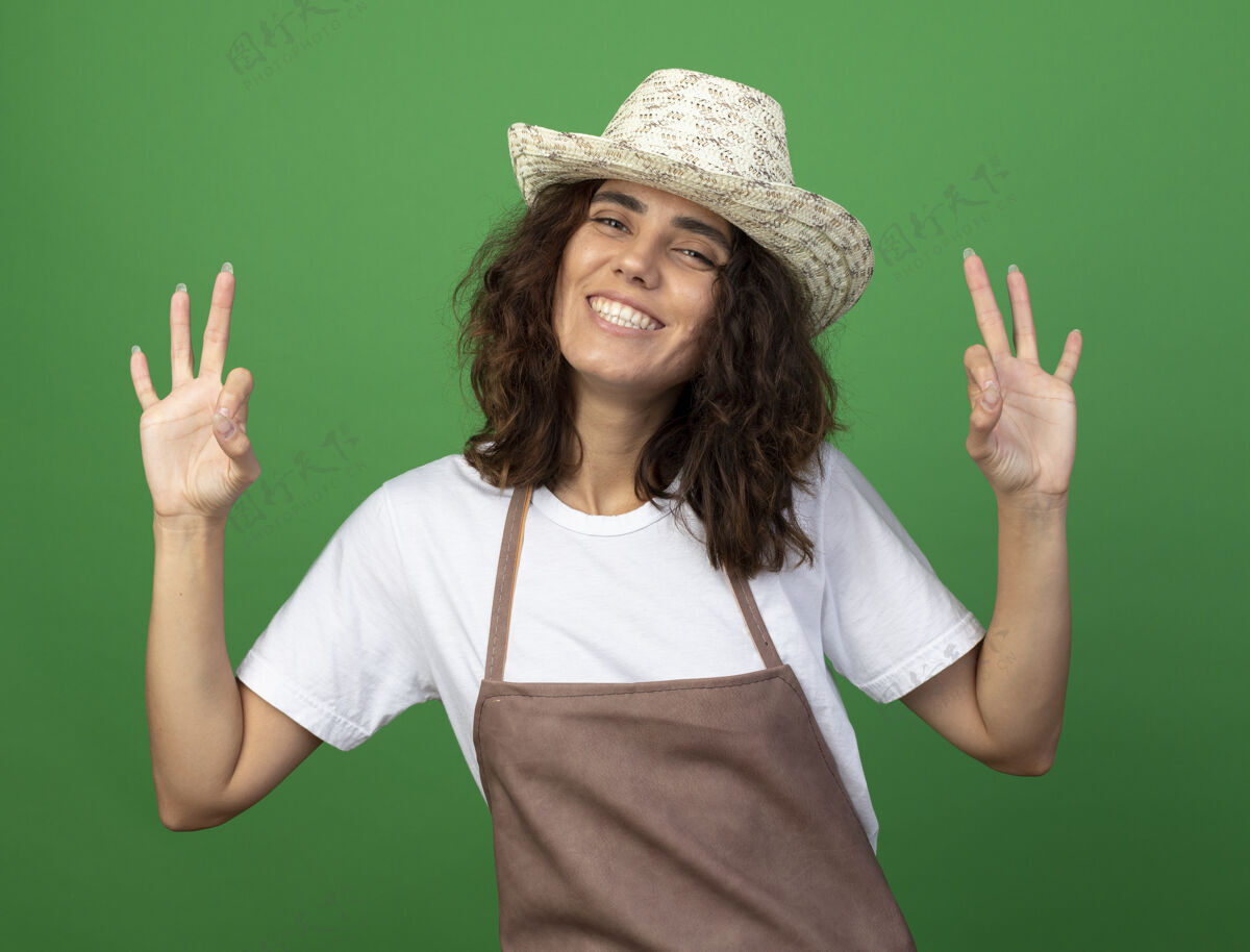 年轻身着制服的年轻女园丁微笑着 戴着园艺帽 在草地上表现出良好的姿态制服花园女性