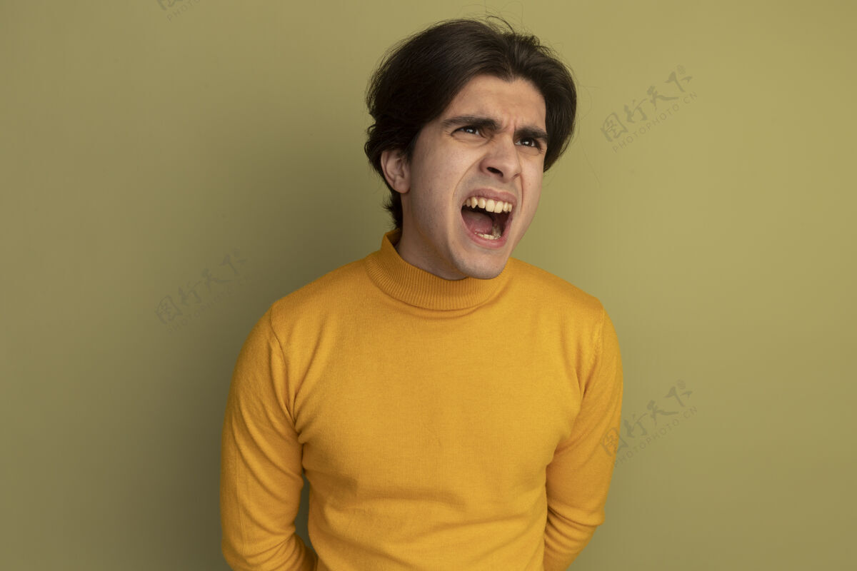 高领毛衣愤怒的看着身边年轻帅哥穿着黄色高领毛衣孤立在橄榄绿的墙上年轻帅哥毛衣