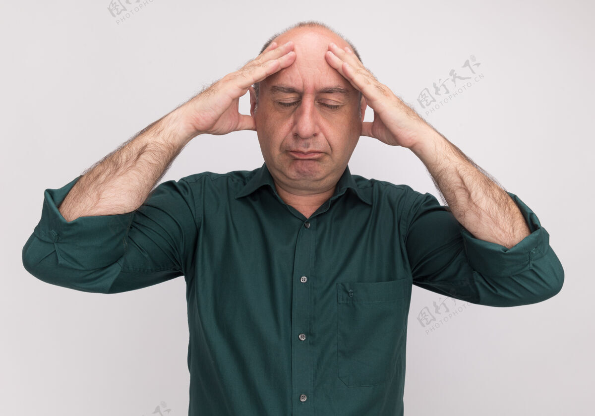 累了厌倦了闭着眼睛的中年男子穿着绿色t恤把手放在额头上隔离在白色的墙上额头戴着手