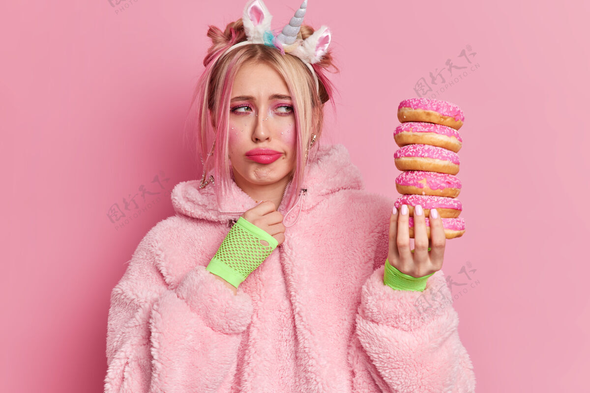 外套心烦意乱的金发碧眼的女人带着明亮的妆容悲伤地看着一堆美味的甜甜圈 觉得想吃点甜食的诱惑外套脸甜甜圈
