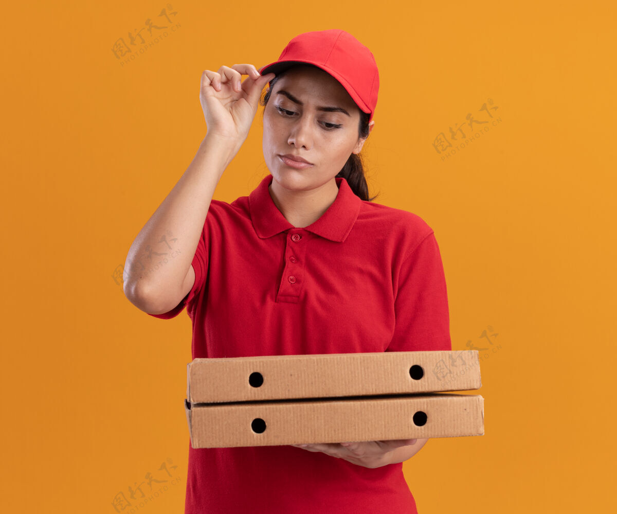 女孩想着那个穿着制服 戴着帽子的年轻送货女孩 看着隔离在橙色墙上的披萨盒 手里拿着帽子披萨穿思考