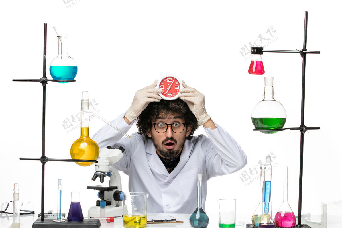 科学前视图穿着医疗服的男科学家拿着红色的时钟在浅白的空间里医学医生套装