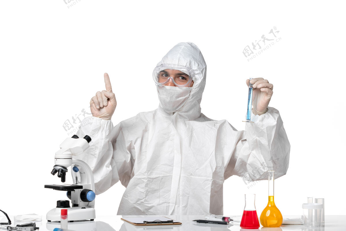 人正面图：男医生穿着防护服 戴着口罩 白色桌子上放着一个装有蓝色溶液的瓶子面罩桌子药品