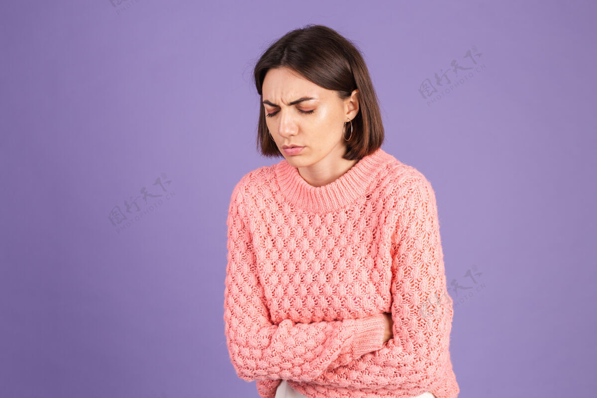 生病穿着粉色毛衣的年轻黑发女郎被隔离在紫色的墙上疼痛黑发抽筋