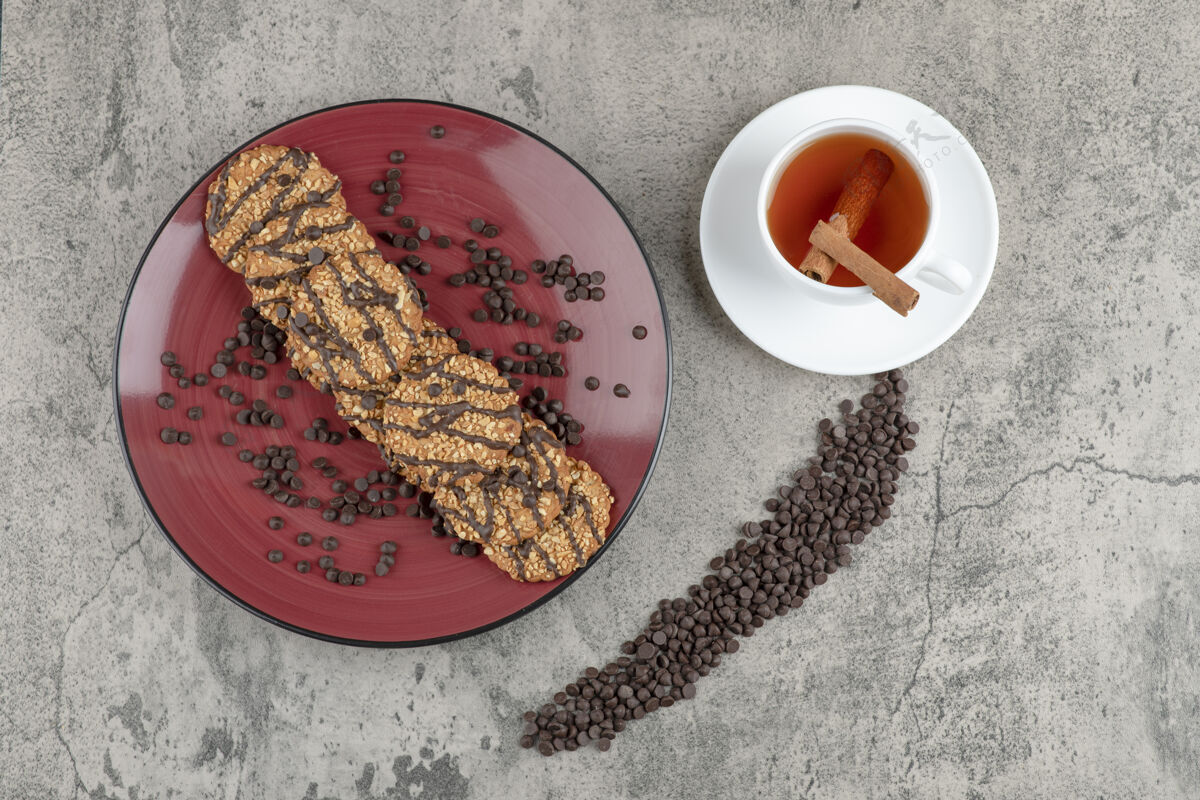 燕麦片美味的饼干撒上巧克力滴在红色盘子和一杯茶饼干热的杯子