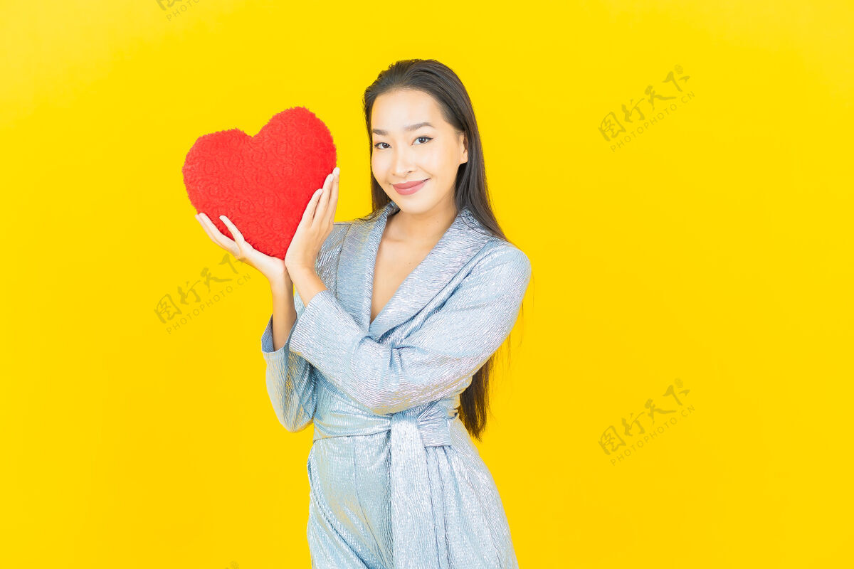 情人节在黄色的墙上画着美丽的亚洲年轻女子微笑的心枕形状人中国标志