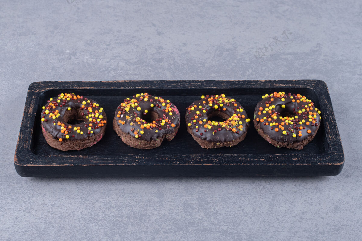 巧克力在大理石表面的盘子上放上巧克力和撒上糖果的甜甜圈外套美味烘焙食品