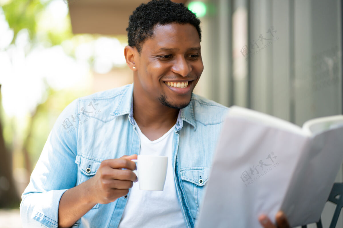 年轻一个非洲裔美国人坐在咖啡馆里放松和看书男性喝酒欢乐