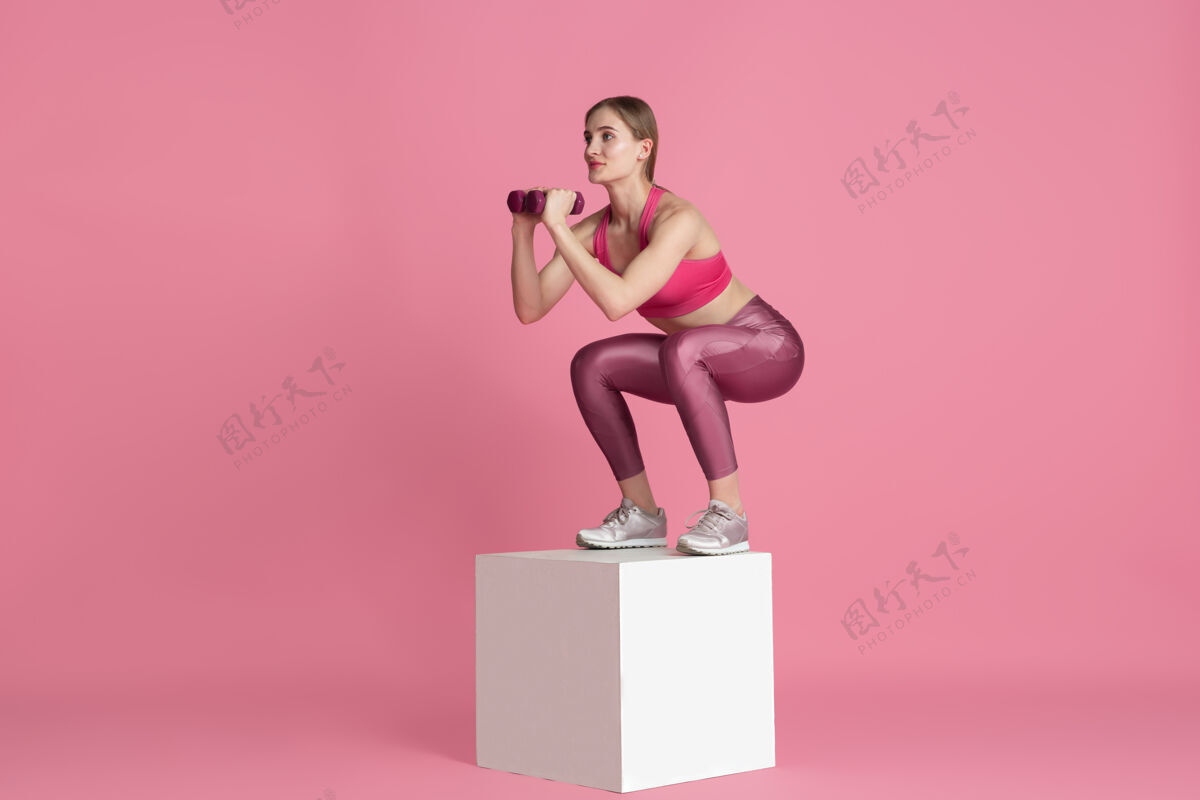 举重美丽的年轻女运动员在粉红色墙上练习单色肖像体重运动装杠铃