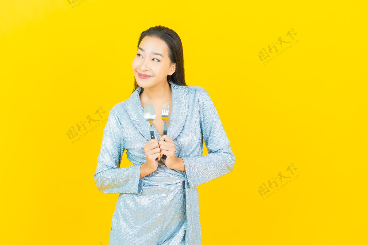 女性画像美丽的亚洲年轻女子微笑着用勺子和叉子在黄色的墙上餐具一欢呼