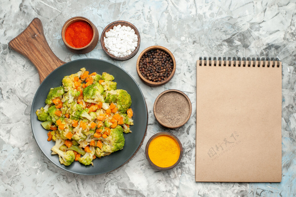 正餐新鲜健康的蔬菜沙拉放在木砧板上 笔记本放在白桌子上烹饪切笔记本