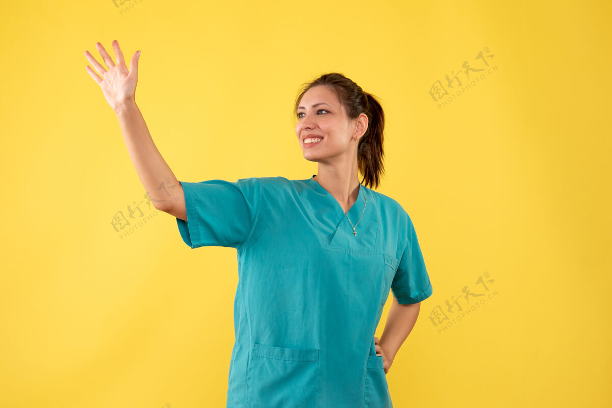 病毒正面图黄色背景下 身着医用衬衫的女医生微笑着挥手致意视图黄色肖像