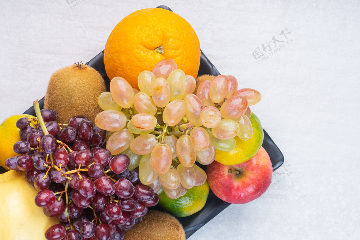 成熟各种美味的水果放在黑色的盘子里 放在大理石上橙子苹果梨