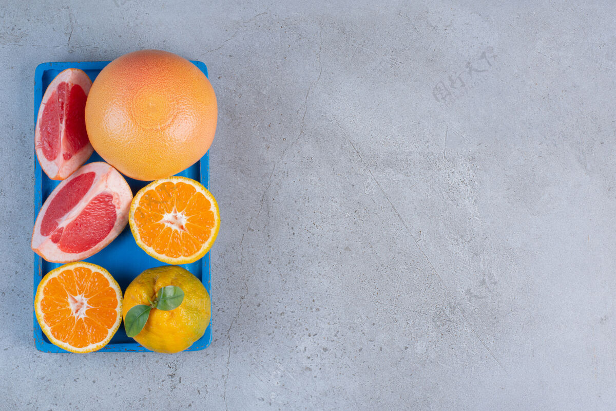 天然把整个橘子和葡萄柚片放在一个蓝色的小托盘上 放在大理石背景上切片美味健康