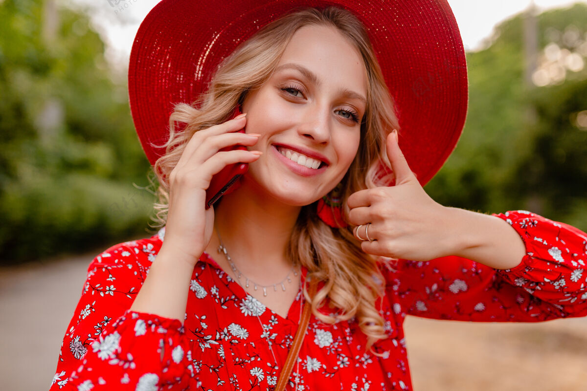 享受迷人的时尚金发微笑的妇女在稻草红色帽子和衬衫夏季时尚服装画像在电话交谈积极的姿态情感白色配饰女性