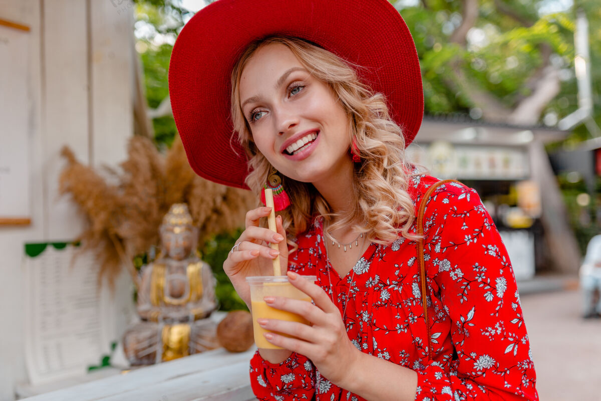 时尚迷人时尚的金发微笑女士 头戴草帽 身穿短衫 夏季时尚套装 饮用天然水果鸡尾酒冰沙女性女孩明亮