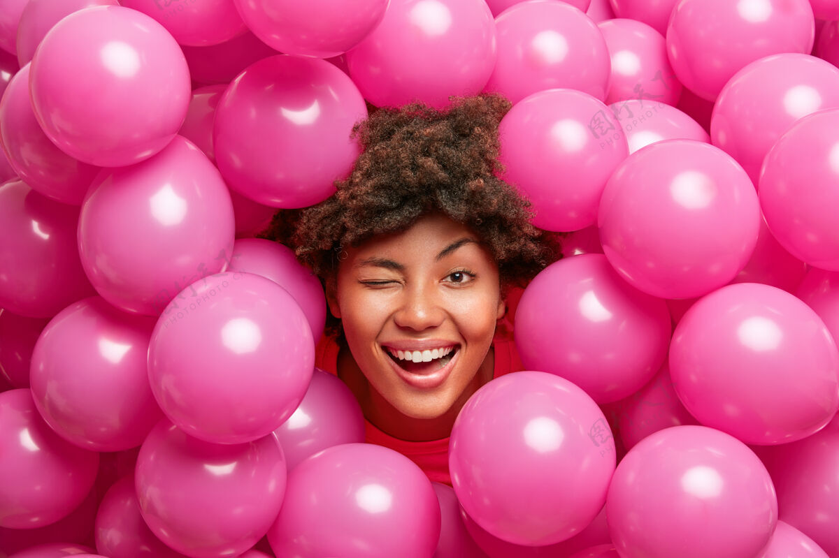 女性乐观的生日女人玩得很开心 眨着眼睛笑着快乐地对着许多粉红色的气球摆姿势女人梦想欣喜若狂