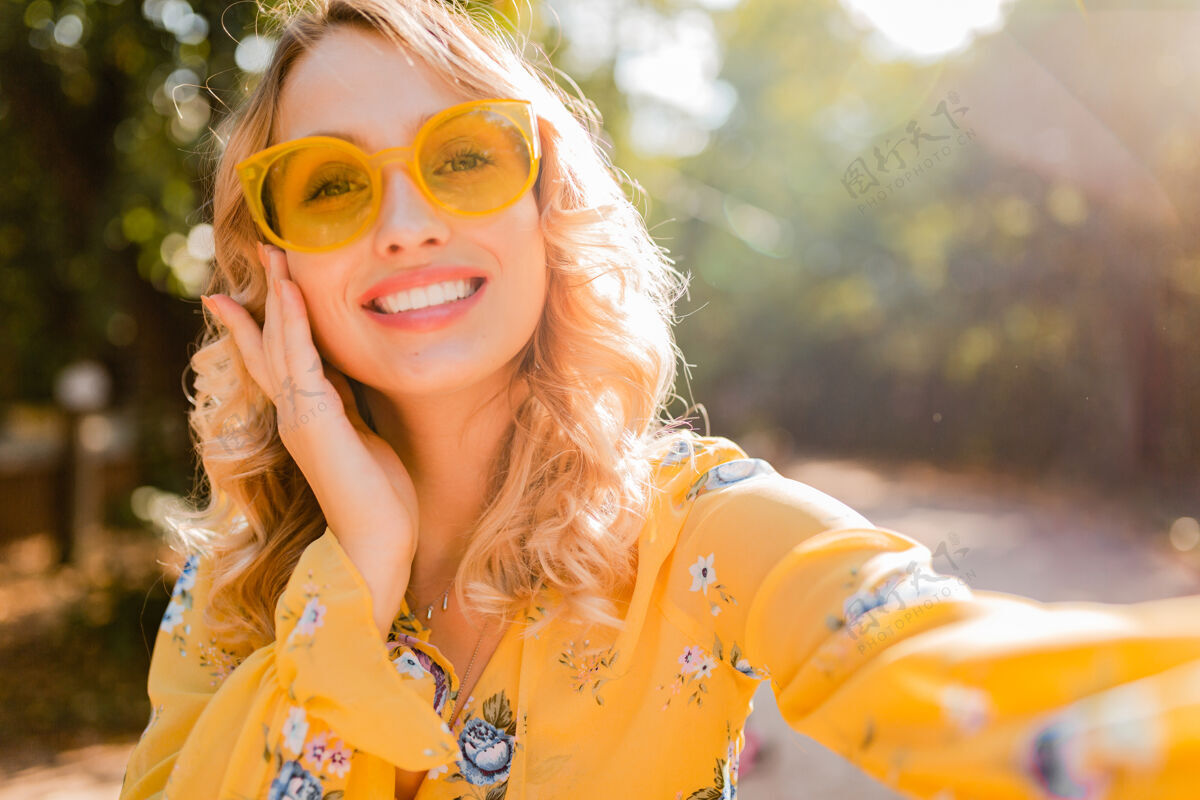 装束美丽的金发时尚微笑的黄色女衬衫戴墨镜自拍照片的肖像欢呼太阳镜女士
