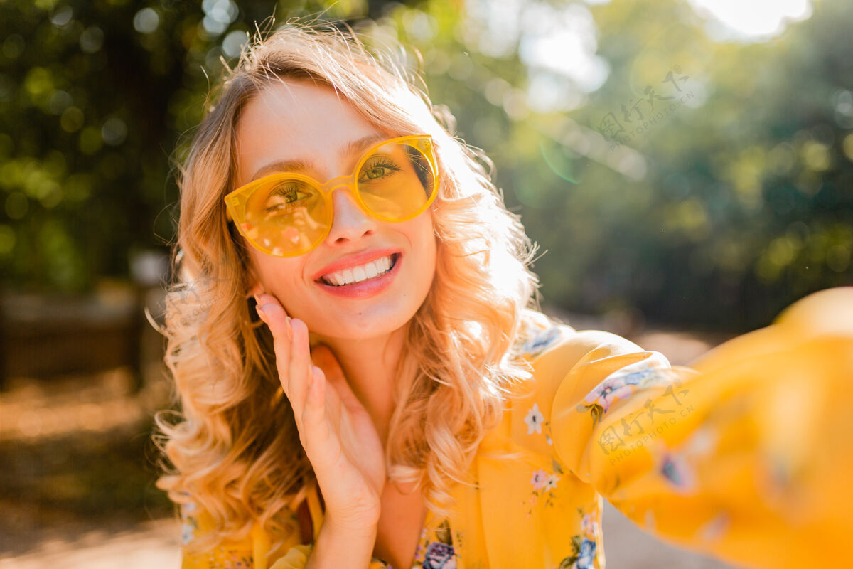酷美丽的金发时尚微笑的黄色女衬衫戴墨镜自拍照片的肖像配饰黄色女人