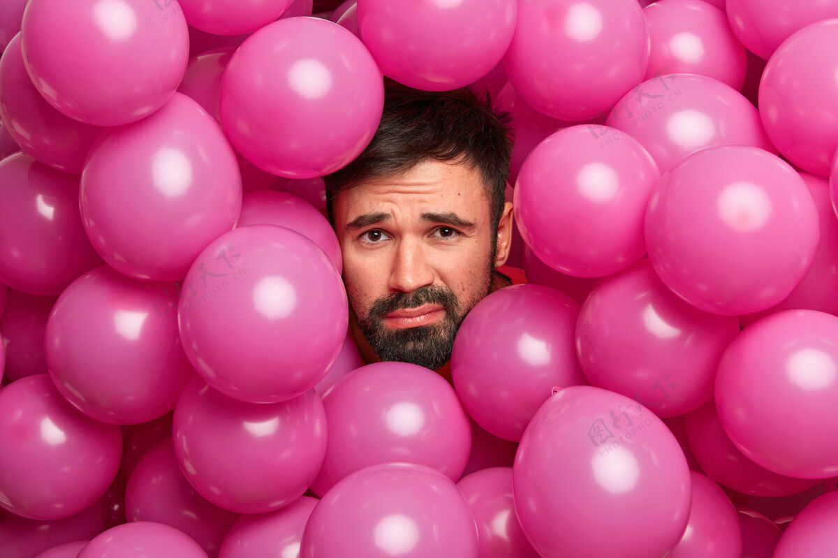 颜色不满的留着胡子的欧洲男人在安排完生日派对后累了 围着许多粉红色的气球摆姿势庆典不刮胡子人
