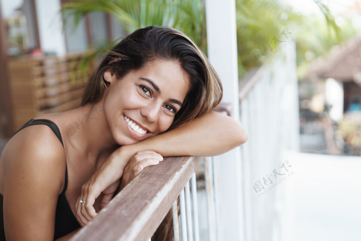 享受快乐漂亮的年轻晒黑的女人倚在露台的栏杆上 快乐地凝视着假期放松休闲