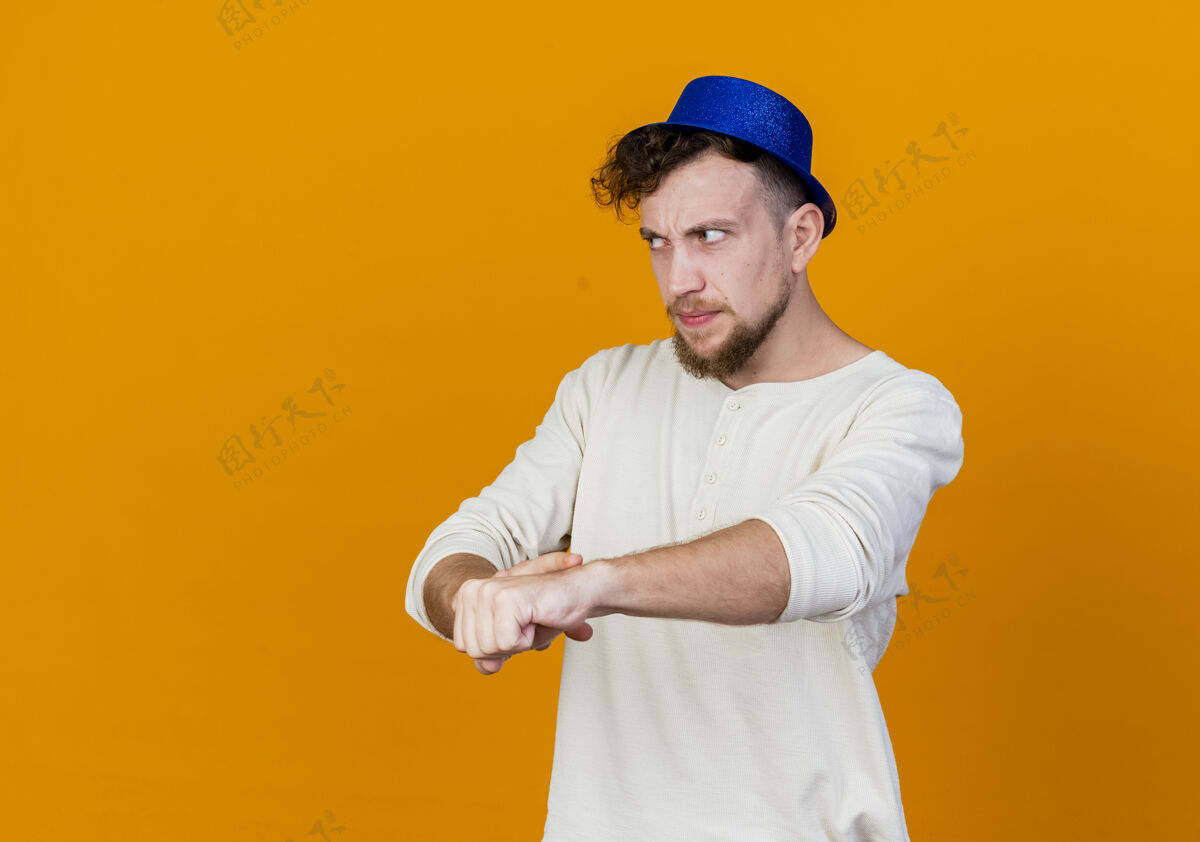 假装未发布的年轻英俊的斯拉夫党家伙戴着党的帽子直看做你迟到的手势橙色背景与复制空间孤立直率空间年轻
