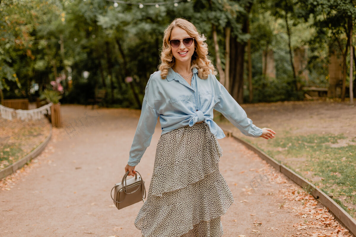 时尚迷人的金发微笑的女人穿着夏天的行头走在公园里包休闲衣服