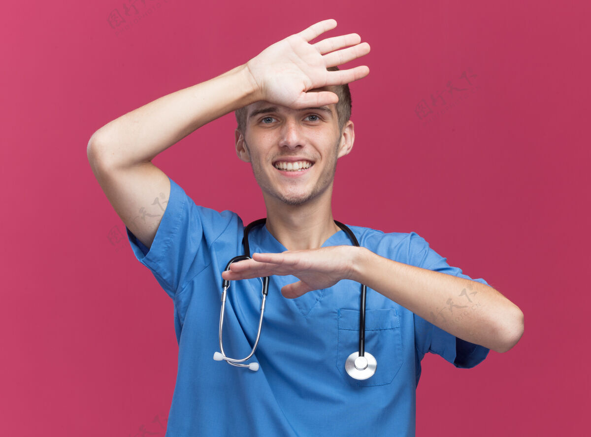 微笑面带微笑的年轻男医生穿着医生制服 手放在隔离在粉红色墙上的前额上 戴着听诊器医生听诊器男性