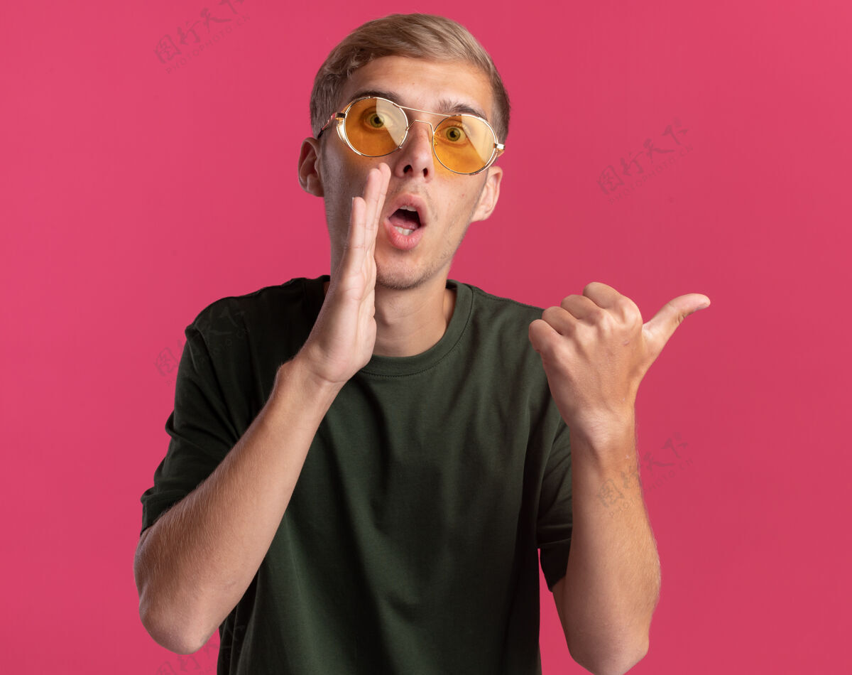 穿可疑的年轻帅哥穿着绿色衬衫 戴着眼镜低声说 并指出在粉红色的墙壁与复制空间隔离侧可疑眼镜壁板
