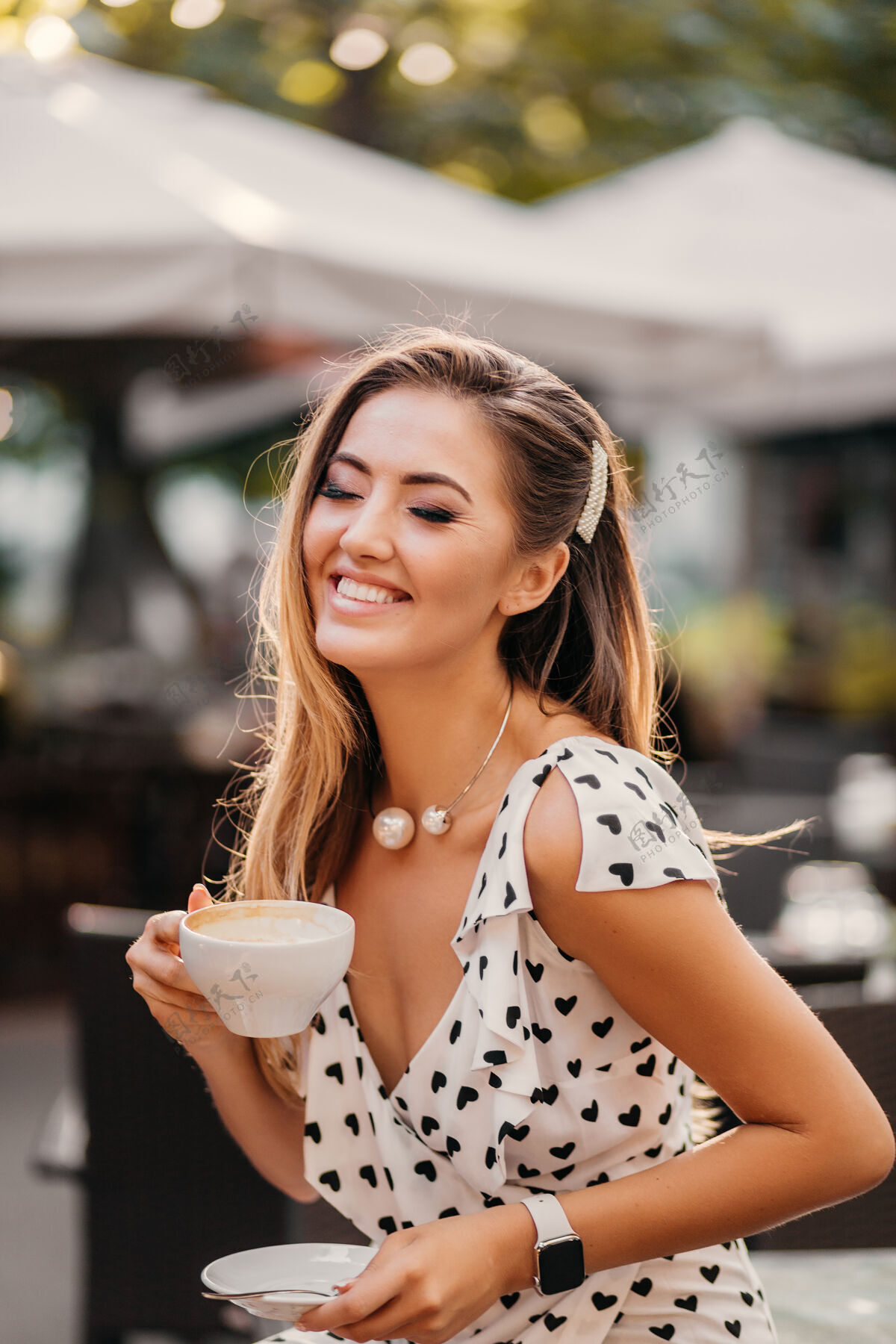 积极美丽的女人带着坦诚的微笑坐在夏日咖啡馆里笑着 手里拿着一杯卡布奇诺性感灯光女性