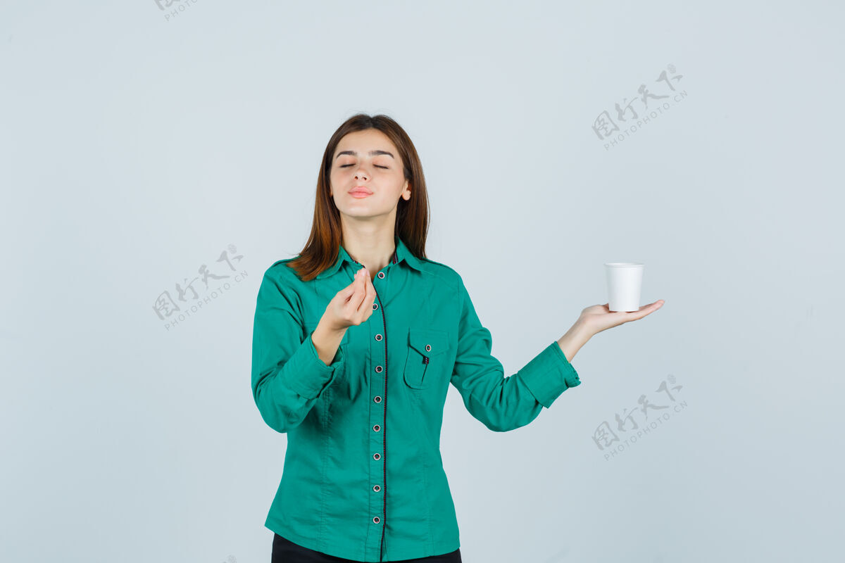 杯子年轻的女士手里拿着一杯塑料咖啡 一边在衬衫上摆出美味的姿势 神情愉悦 俯瞰前方微笑时尚咖啡