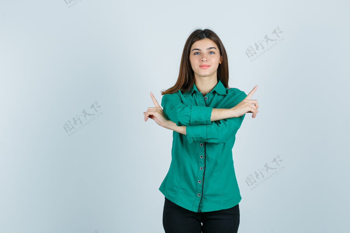 衬衫年轻女孩双臂交叉 食指指向相反的方向 穿着绿色上衣 黑色裤子 看起来很高兴前视图女性头发女人