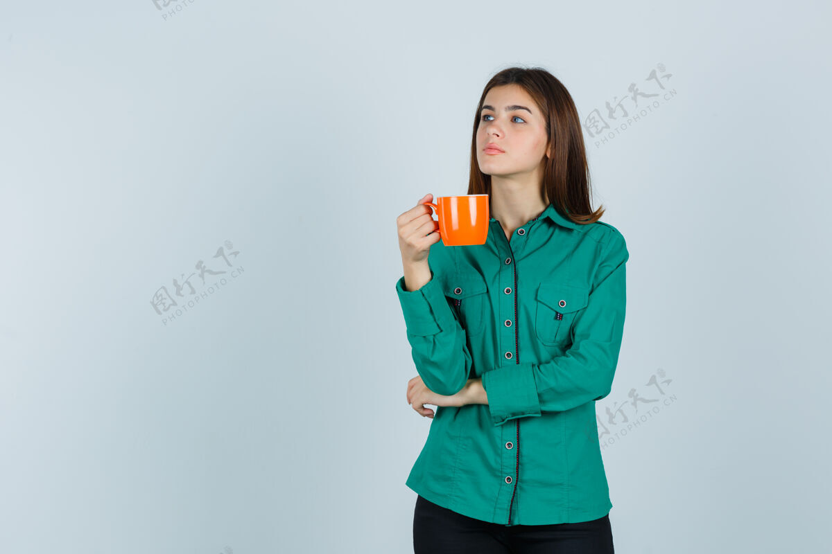 美丽年轻的女士拿着一杯橘色的茶 穿着衬衫 神情沉思 俯瞰前方衬衫乐趣放松
