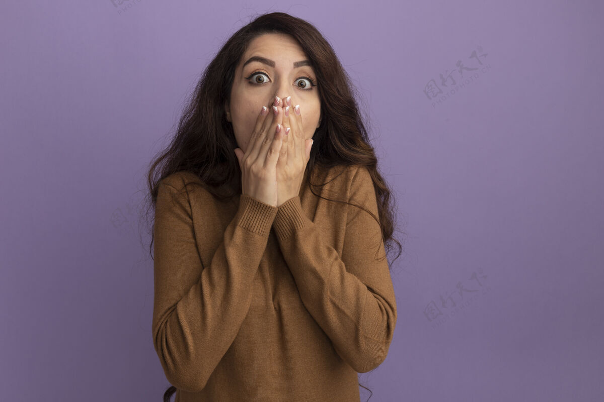 高领毛衣吓得年轻漂亮的女孩穿着棕色高领毛衣 脸上蒙着紫色的隔离墙上的手盖毛衣年轻