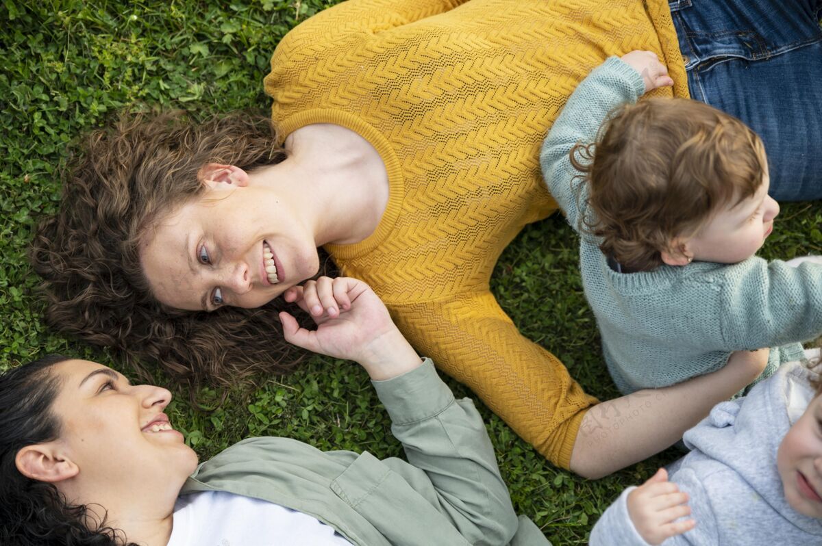婴儿同性恋母亲在公园外面和他们的孩子在草地上放松孩子夫妇水平