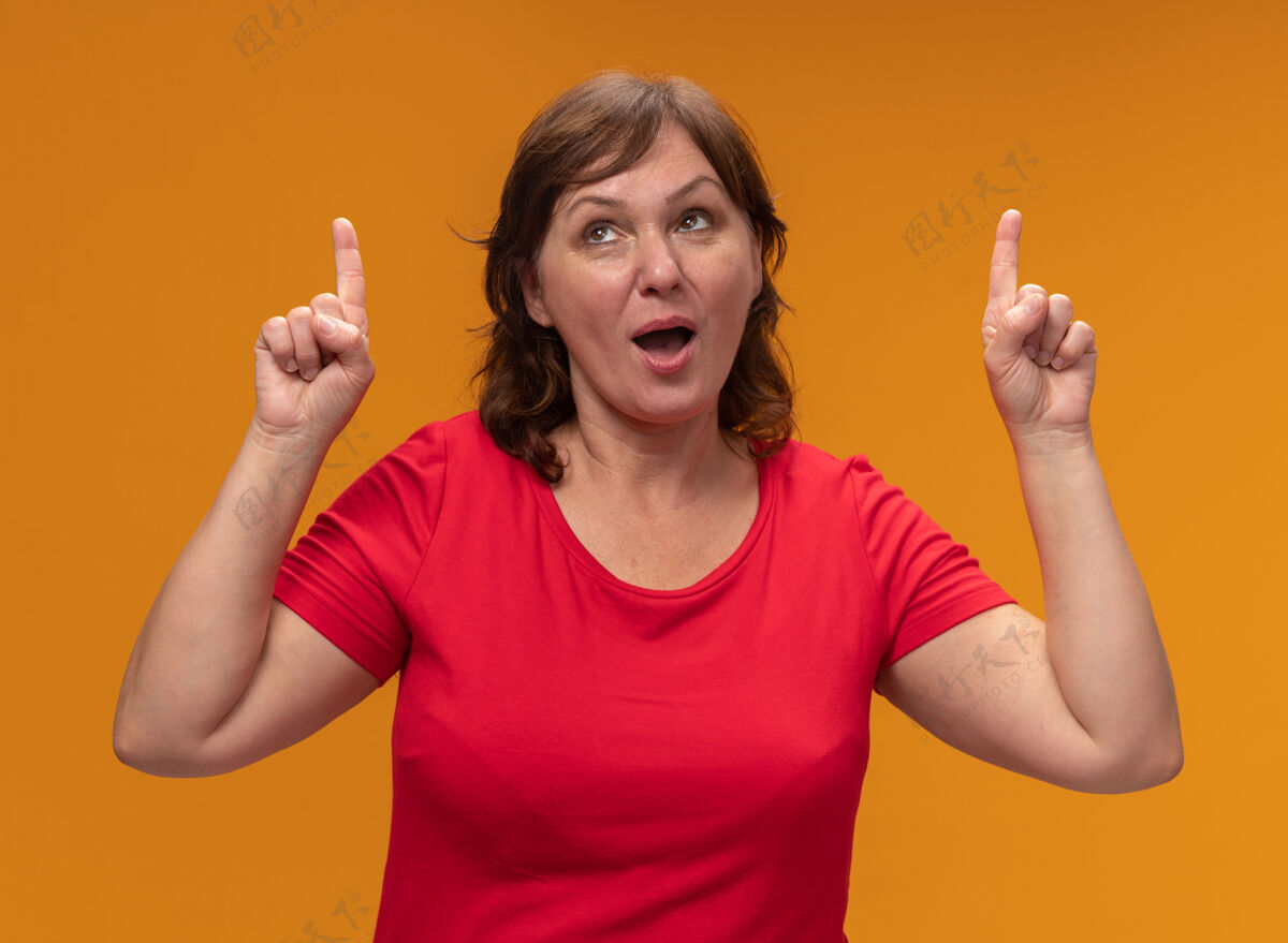 目录身穿红色t恤的中年妇女抬起头微笑着用食指指着站在橙色的墙上中间手指站