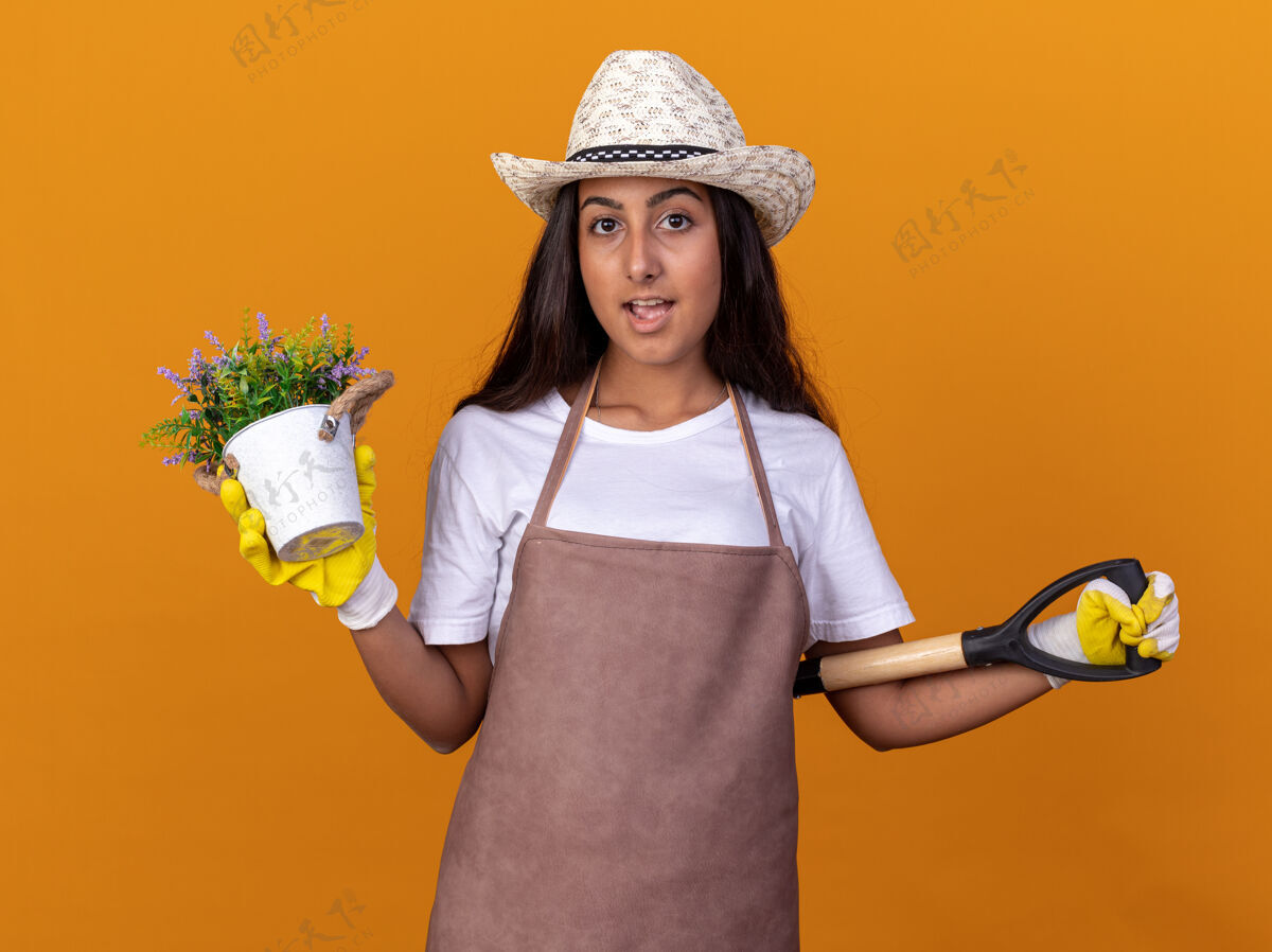 年轻人年轻的园丁女孩拿着盆栽和铲子 脸上带着微笑站在橙色的墙上微笑锅铲子