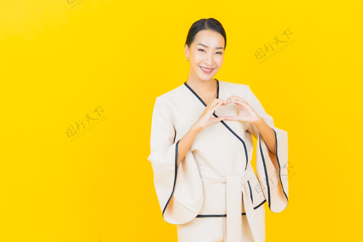 手臂美丽的亚洲年轻商业女性在黄色墙上穿着白色西装微笑的画像脸模特人