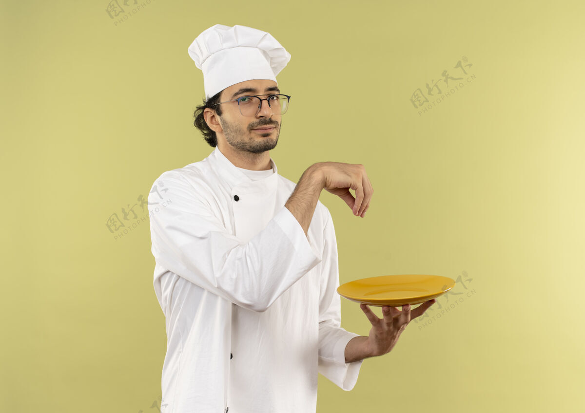 男人年轻的男厨师穿着厨师制服戴着眼镜拿着盘子假装撒盐年轻眼镜烹饪