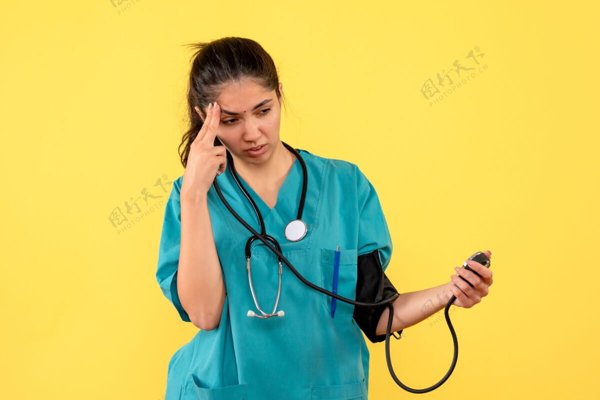 医院正面图：穿着制服的女医生拿着血压计站在黄色背景上医学健康前方